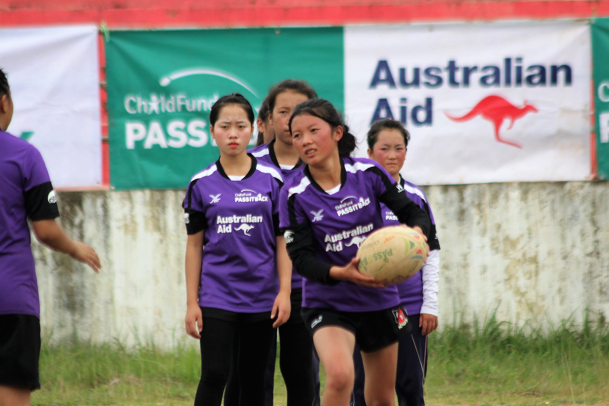 Lar runs with rugby ball while her team mates watch