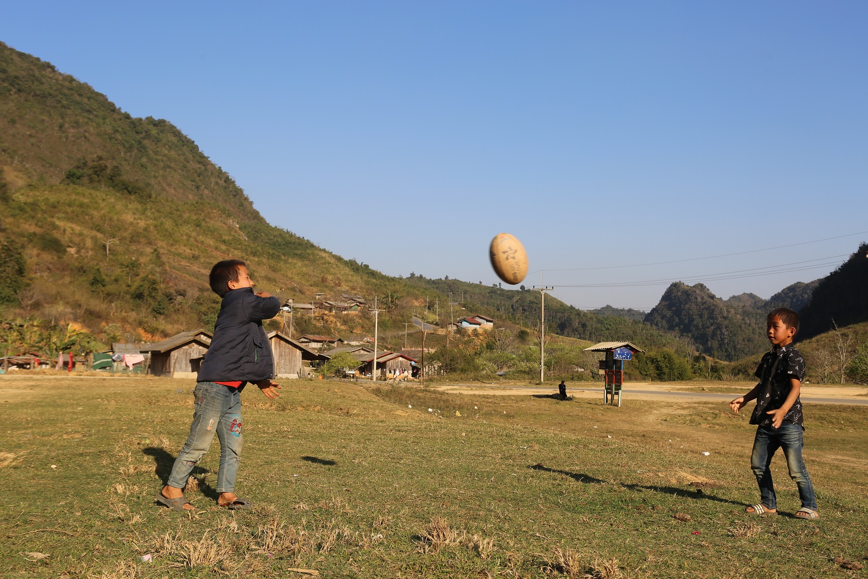 Two boys in a rural area throw a rugby ball to each other 